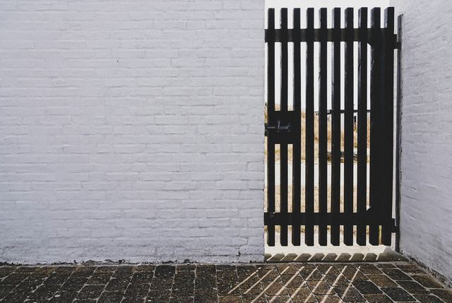 Zwarte tuinpoort met verticale spijlen in een witgeschilderde muur