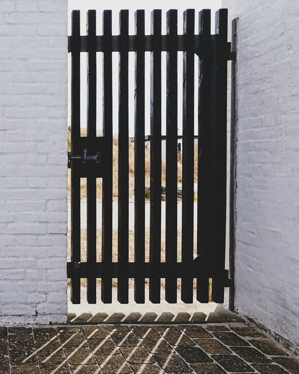 Zwarte tuinpoort met verticale spijlen in een witgeschilderde muur