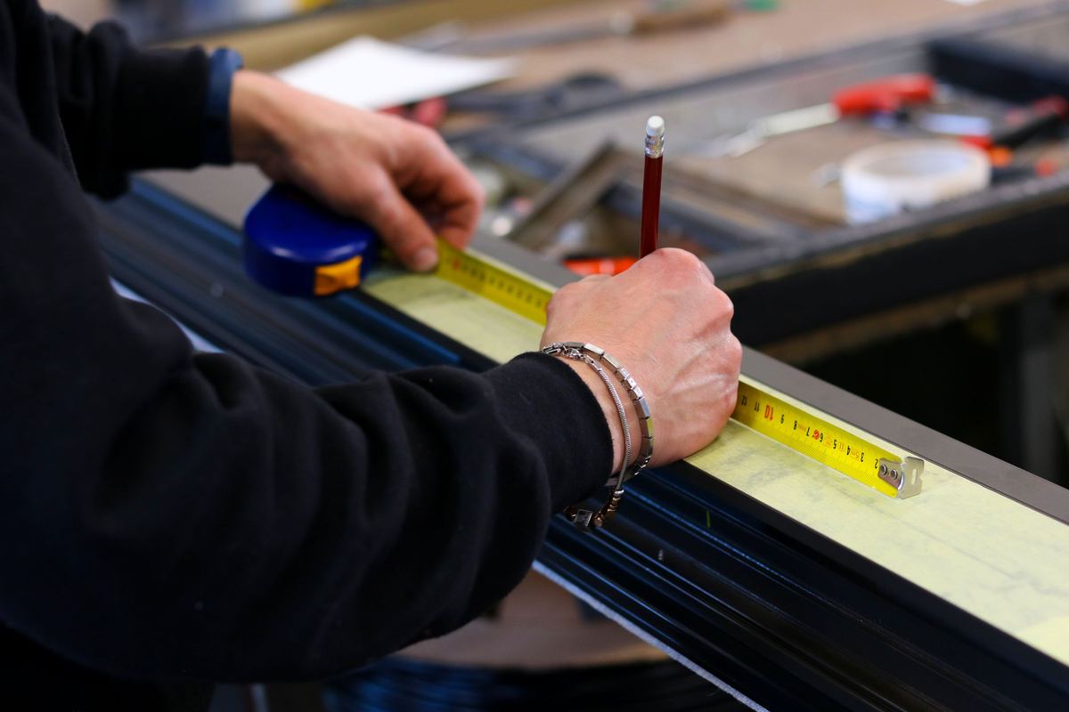 Iemand meet een donker aluminium profiel op met een rolmeter en een potlood